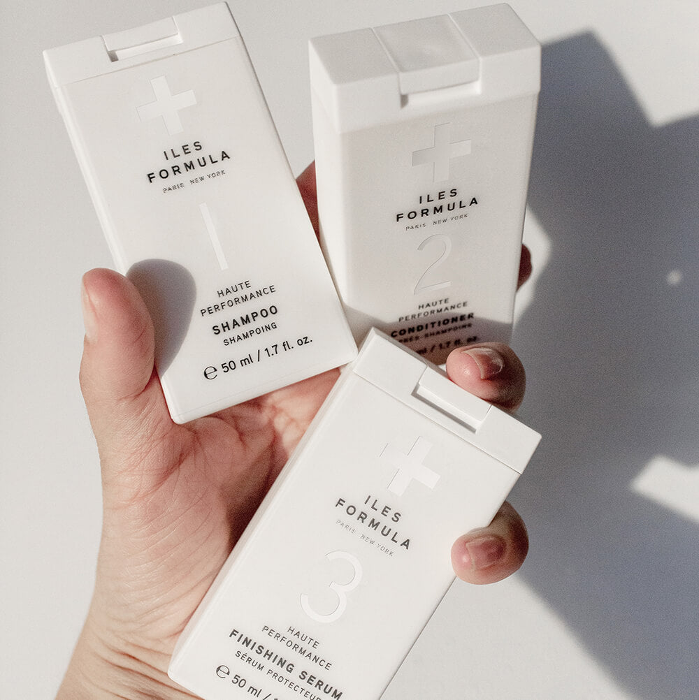 A Hand Holding The Mini Signature Collection; Shampoo, Conditioner, and Finishing Serum